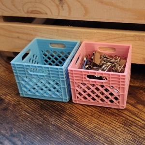 some 3D prints of mini milk crates; one of them has office supplies in it